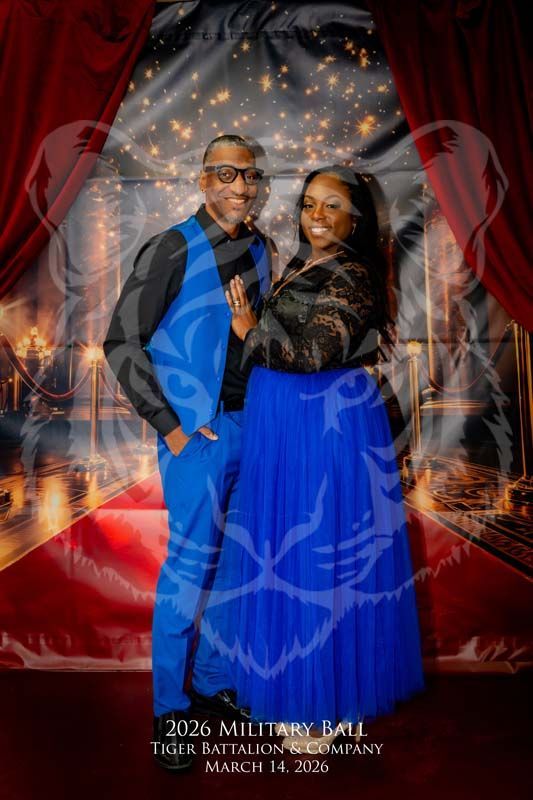 A couple poses for a photo at a formal ball with a red carpet and curtain backdrop and a tiger logo overlay.