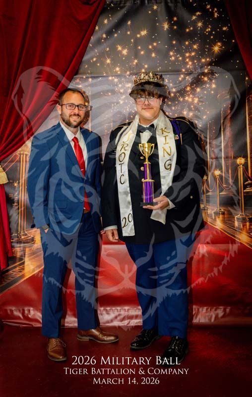 Two people at a 2026 military ball; one wears a suit, the other a uniform with a crown, sash, and trophy.