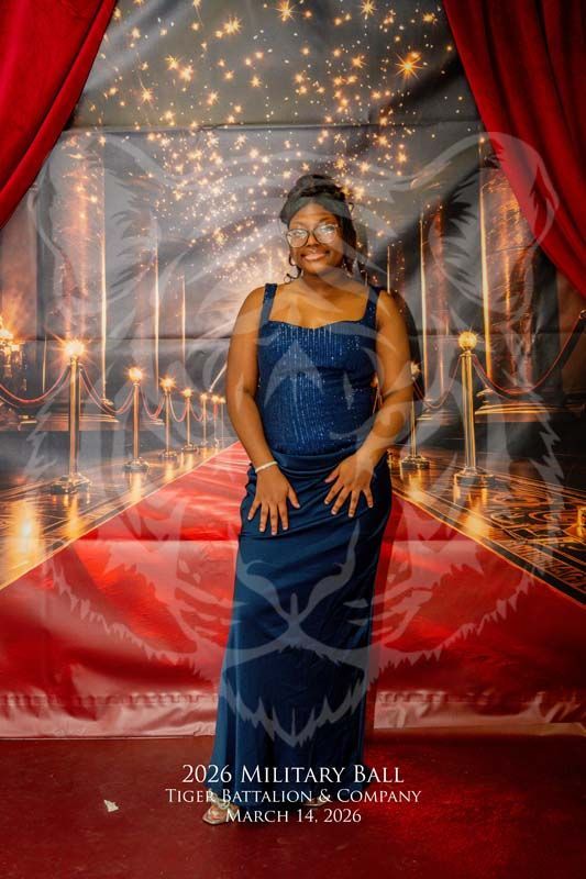 A person in a blue evening gown poses on a red carpet backdrop at a 2026 military ball.