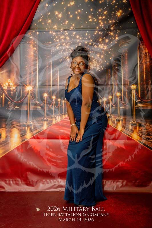 A person in a blue formal dress poses on a red carpet backdrop at the 2026 Tiger Battalion Military Ball.