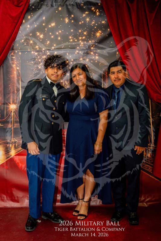 Three people pose for a portrait in front of a red-curtained backdrop with string lights at a Military Ball.
