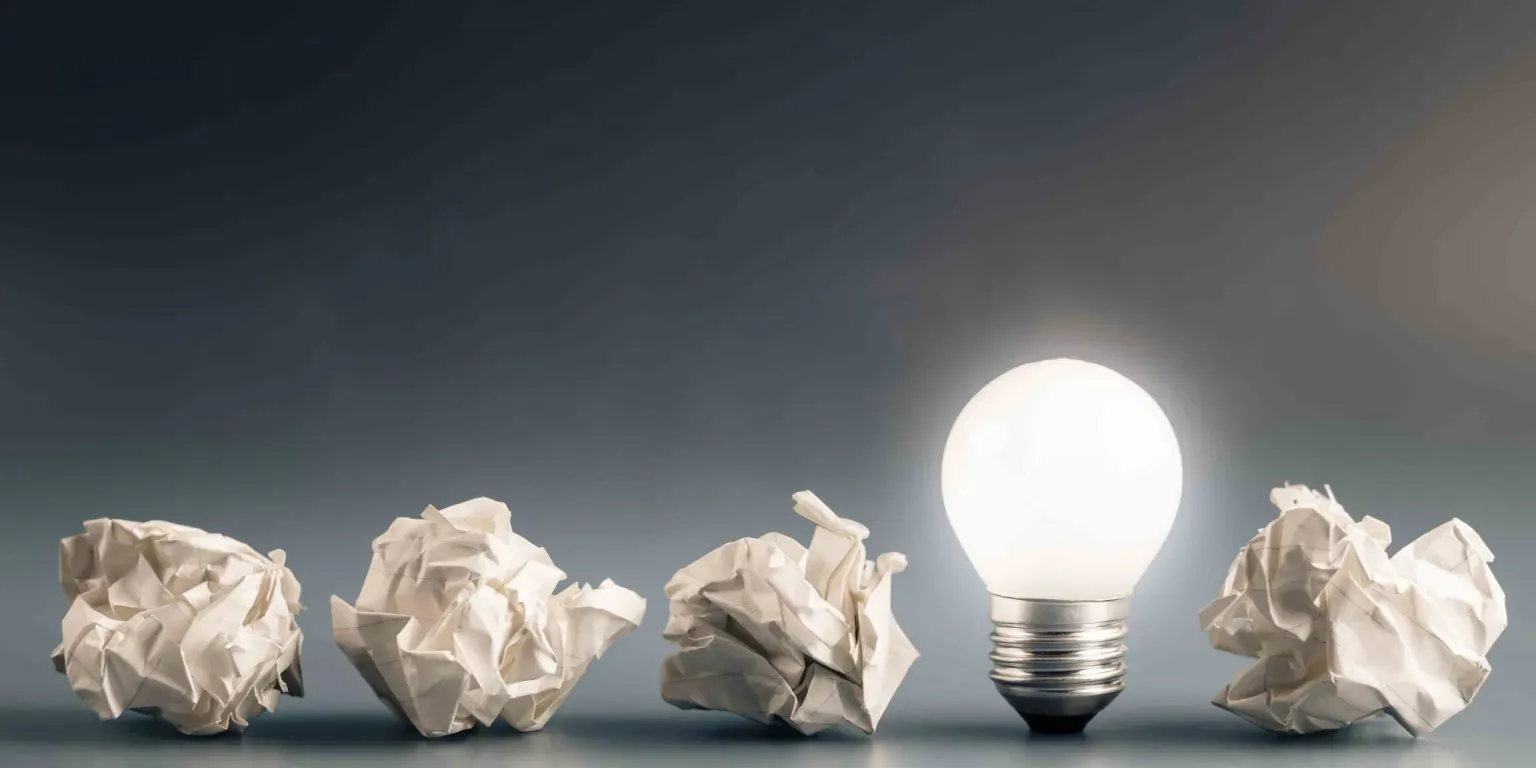 A light bulb is surrounded by crumpled paper balls.