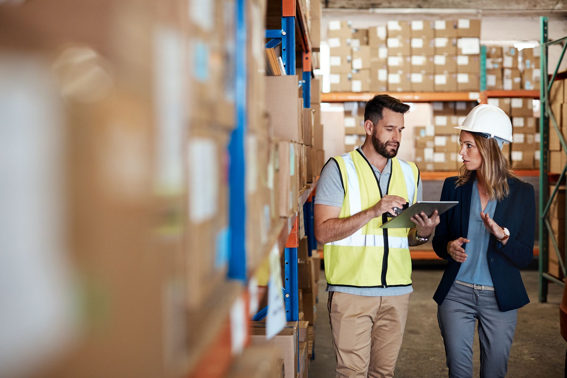 A man and a woman are looking at a tablet in a warehouse.