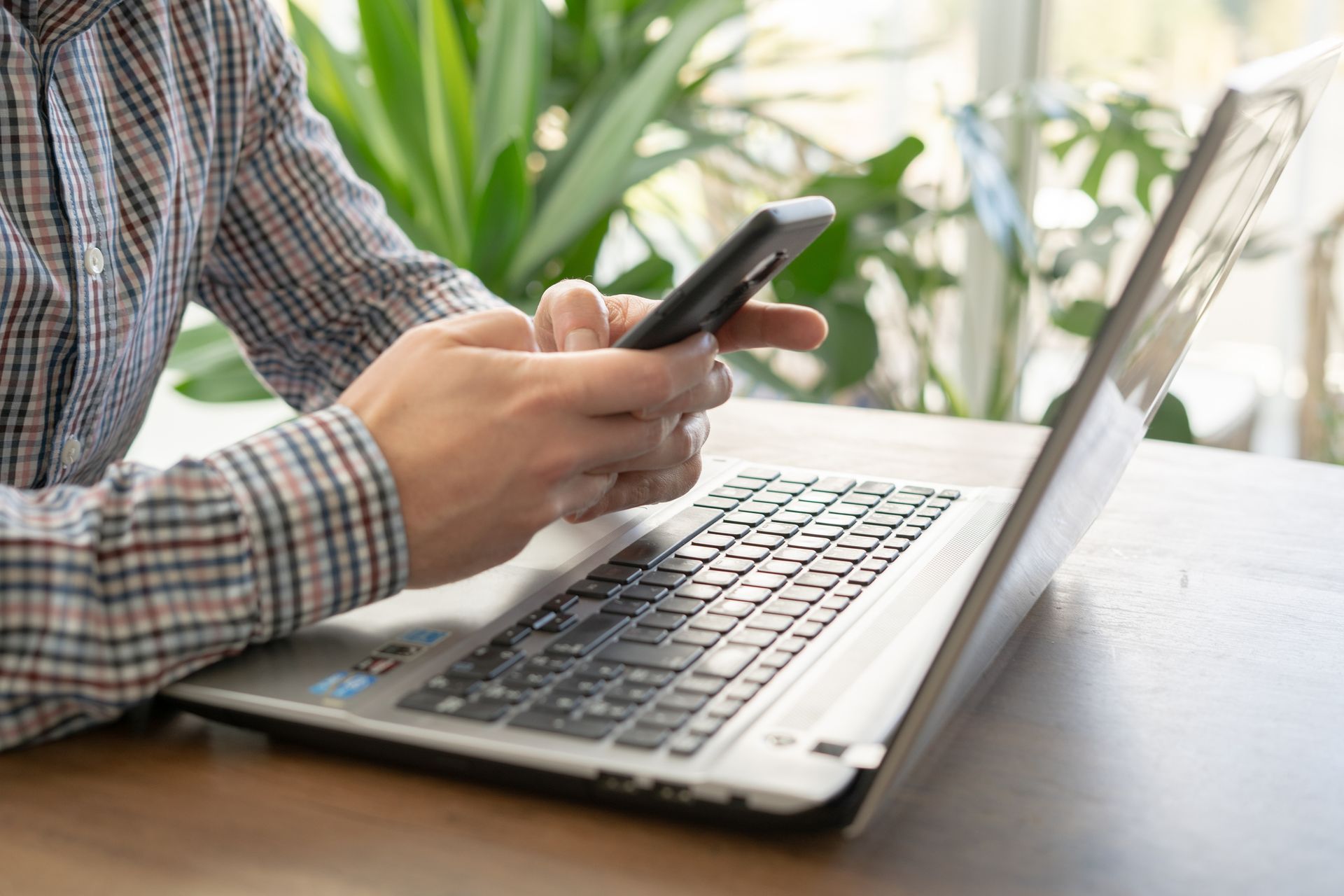 A man is sitting at a table using a laptop and a cell phone.
