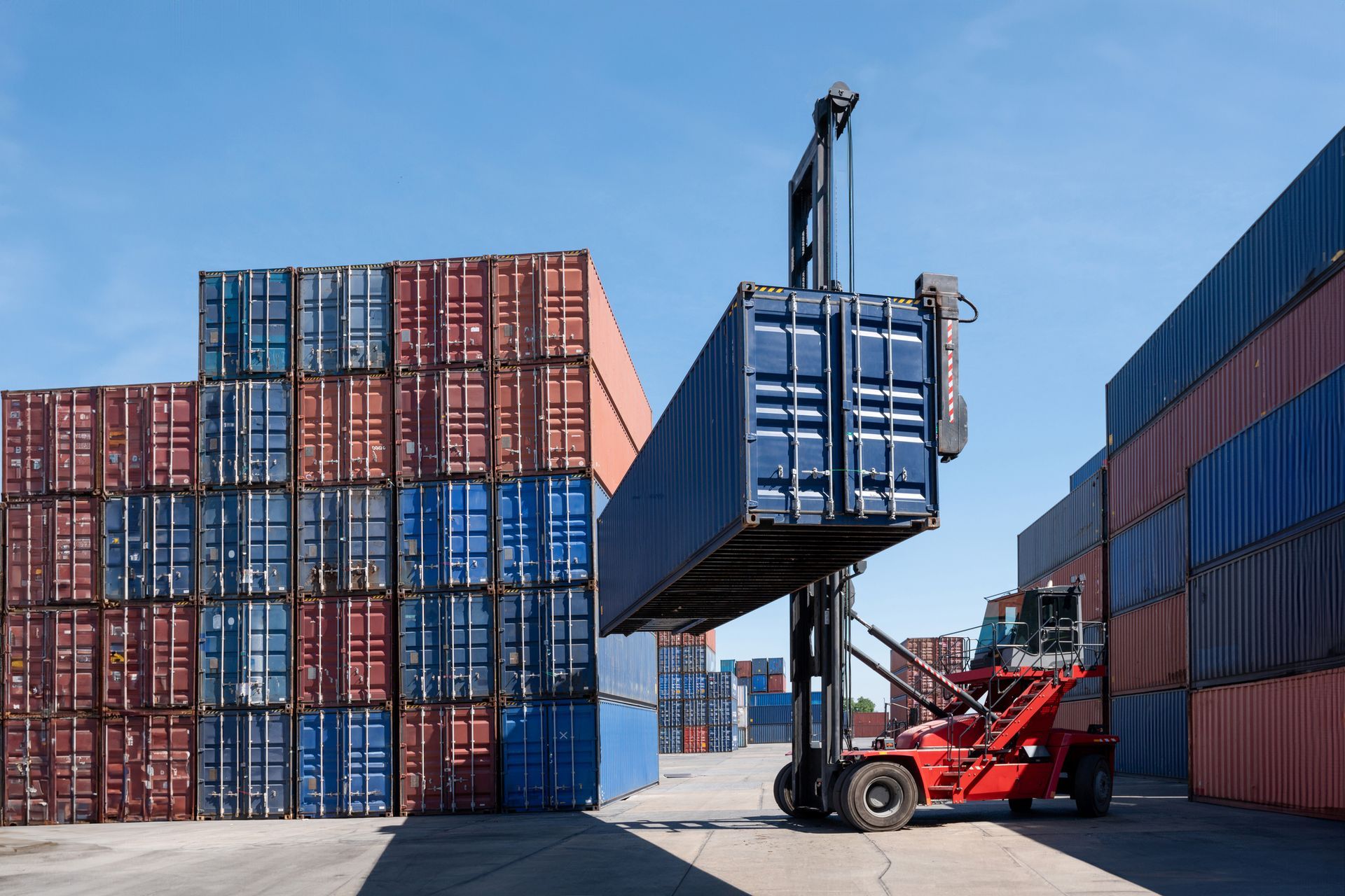 A forklift is lifting a shipping container in a warehouse.