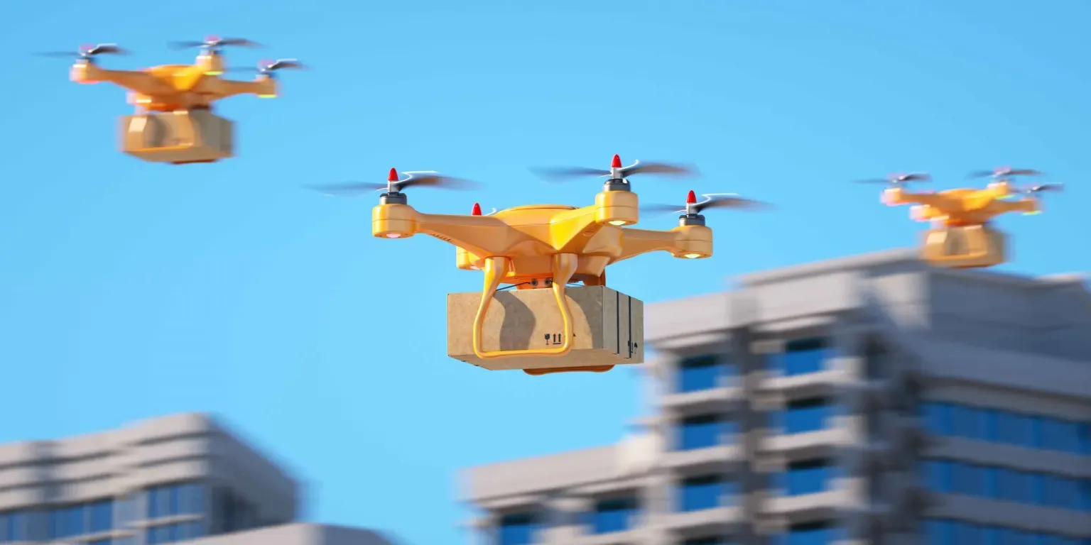 Three drones are flying over a city carrying boxes.