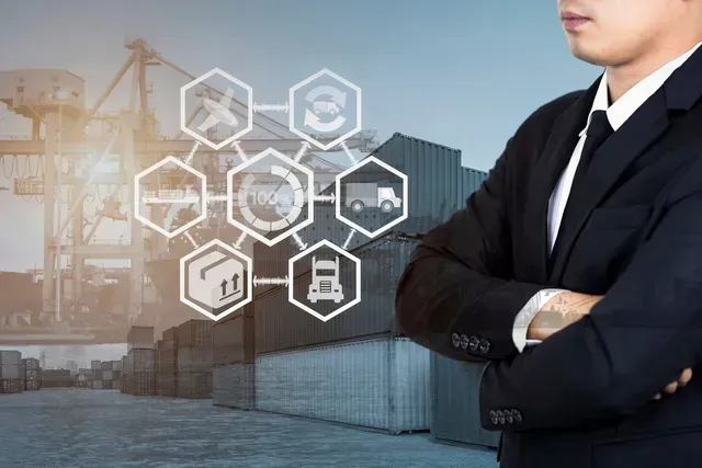 A man in a suit and tie is standing with his arms crossed in front of a warehouse.