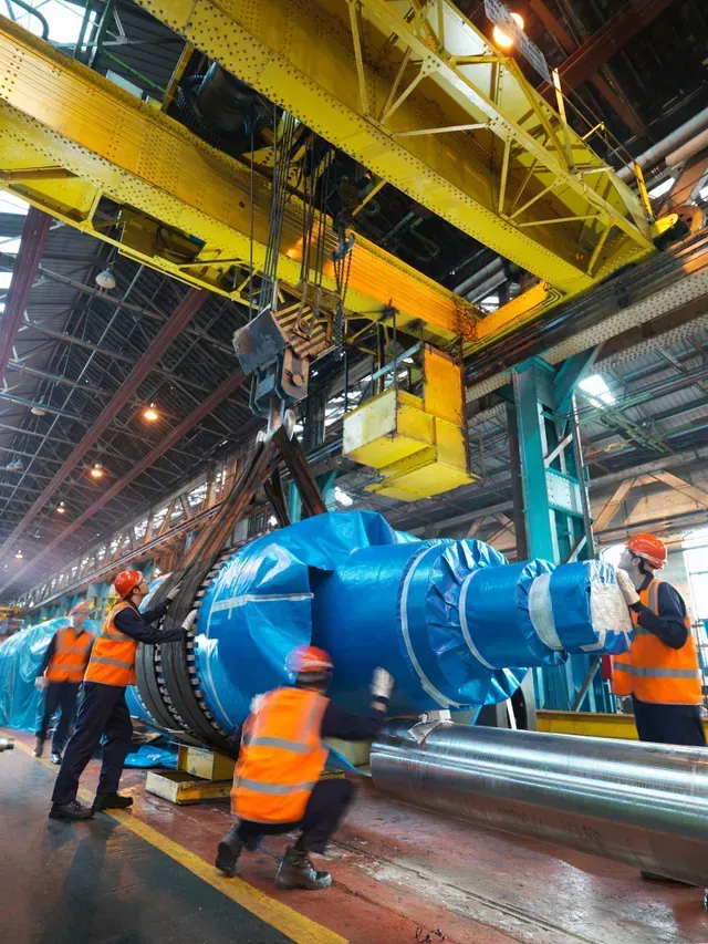 A large blue object is being lifted by a crane in a factory.