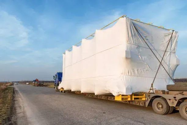 A semi truck is carrying a large object wrapped in plastic.