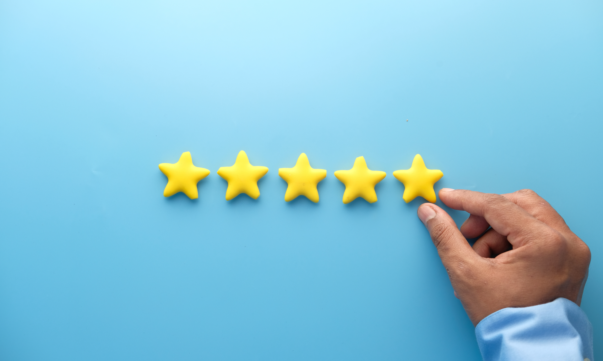 Hand placing a yellow star next to four other yellow stars on a blue surface.