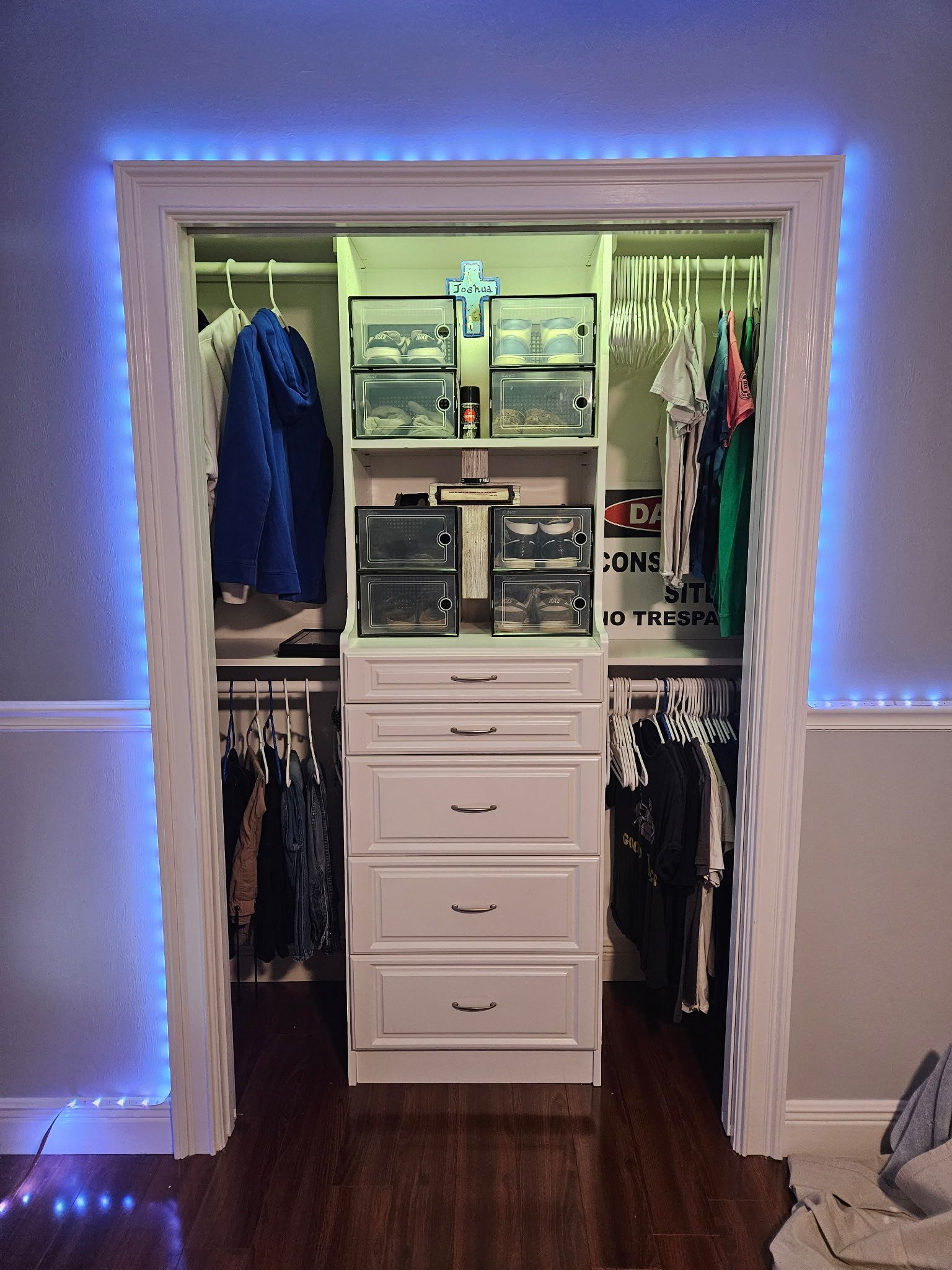 Closet organization with white drawers and shelves, clothes hanging, and blue LED strip lighting around the door frame.