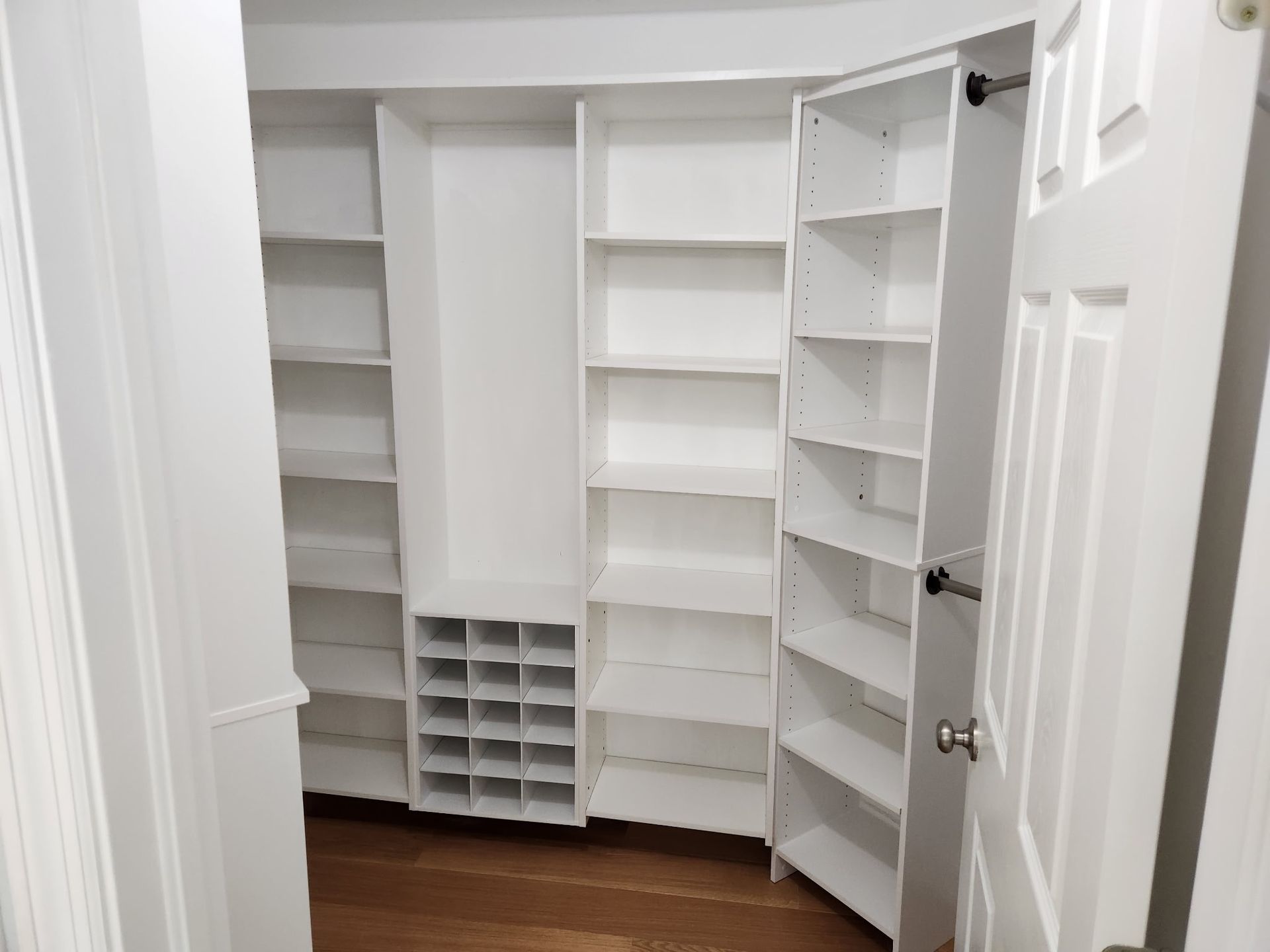 White built-in closet with various shelves and a shoe cubby. A door is slightly open revealing the interior.