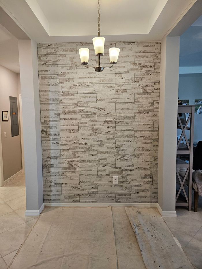 A room with a brick accent wall, a chandelier, and light-colored flooring. 