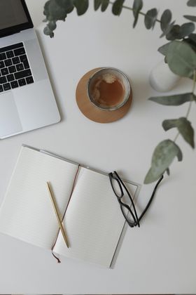 A desk with a laptop a notebook a cup of tea and glasses
