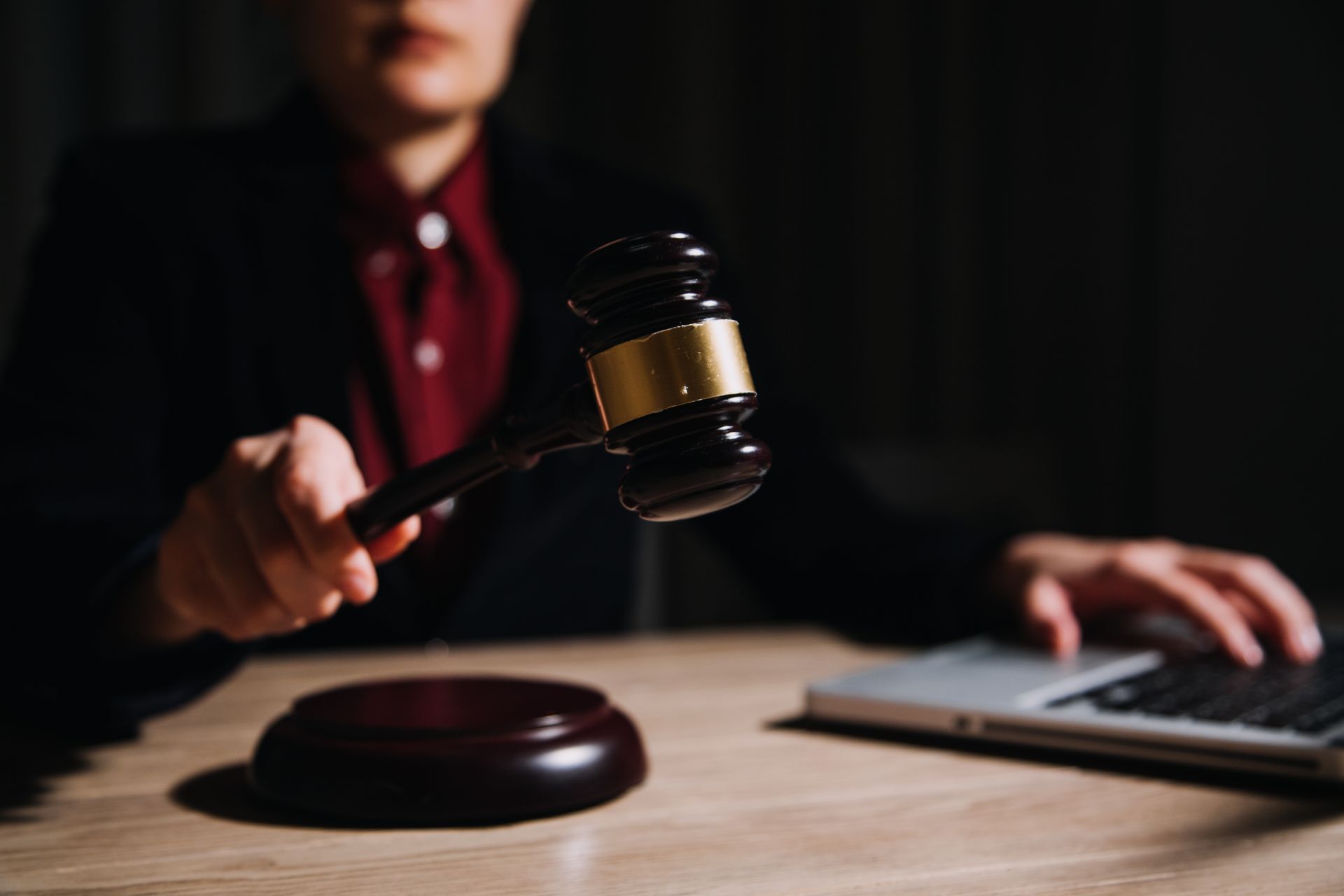 A judge is holding a wooden gavel in front of a laptop computer.