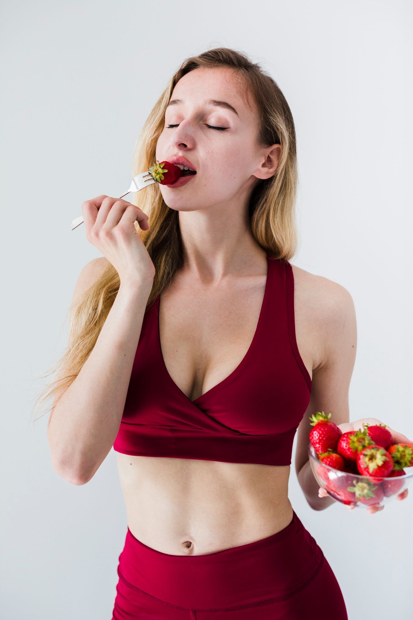 A woman in a red sports outfit enjoying fresh strawberries, symbolizing healthy eating, digestive wellness, and natural energy renewal.
