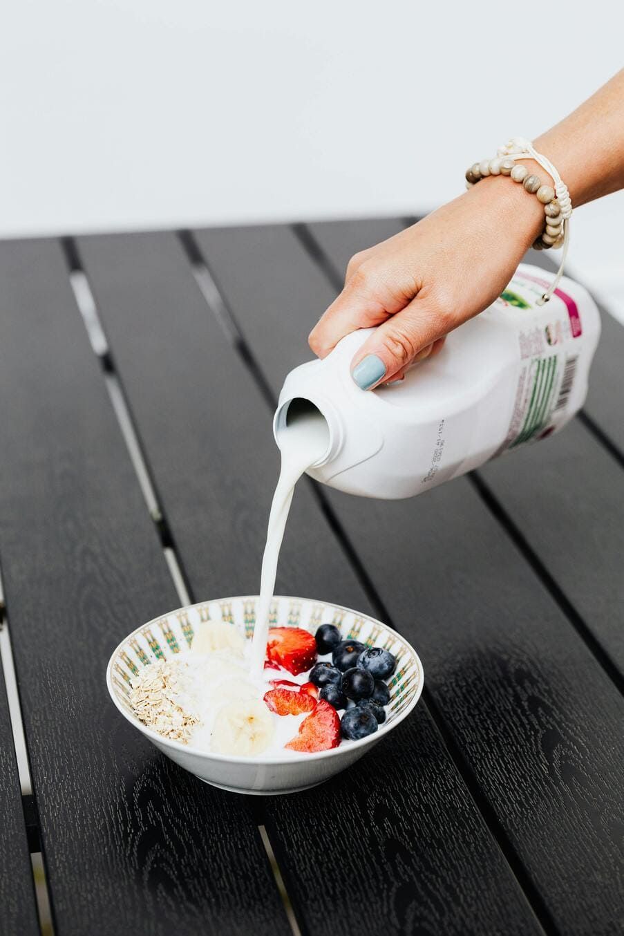a woman pouring milk on the fruit cereal