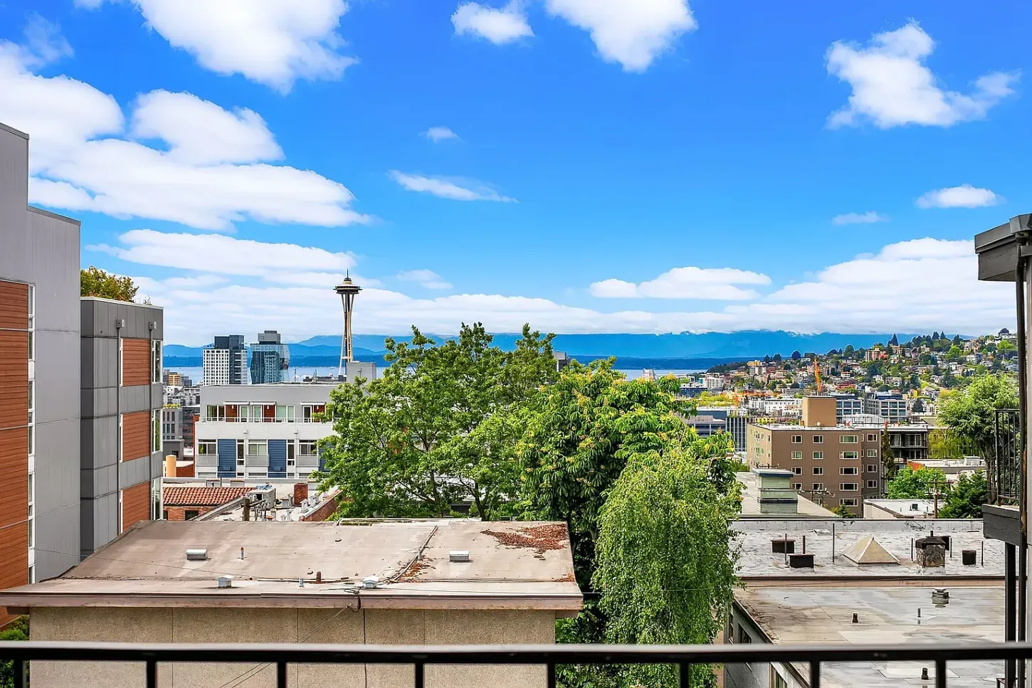 View from a balcony overlooking Seattle's skyline, Space Needle, and Puget Sound, under a blue sky.