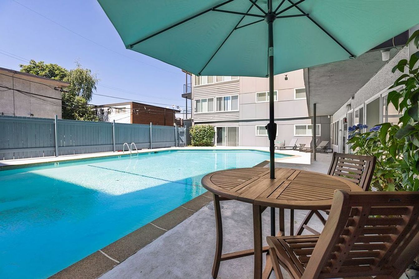 Poolside patio with table and chairs under a teal umbrella, overlooking a swimming pool.