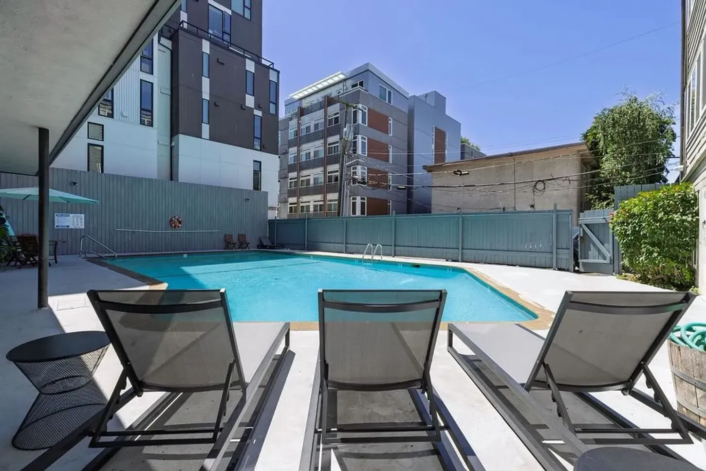 Three lounge chairs face a pool in an outdoor area with modern buildings.