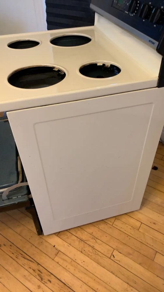 A white stove with four burners is sitting on a wooden floor.