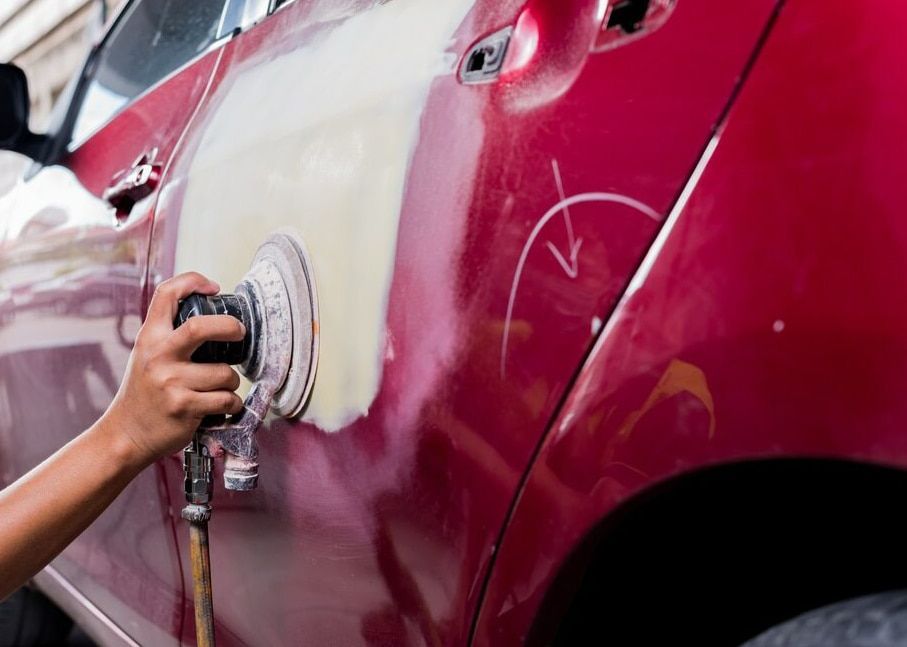 A Person Is Sanding A Red Car With A Sander — Spray Tech Smash Repairs In Gympie, QLD