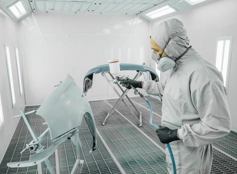 A Man In A Protective Suit Is Painting A Car In A Paint Booth — Spray Tech Smash Repairs In Gympie, QLD
