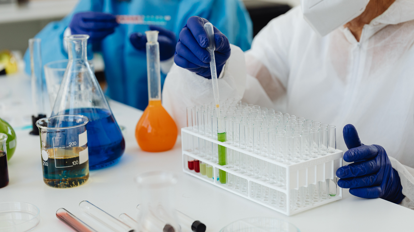Lab workers in protective gear, using pipettes and test tubes with colorful liquids.