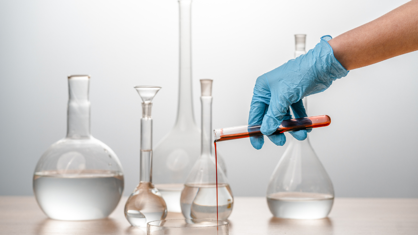 Gloved hand using a pipette with red liquid among laboratory glassware on a lab bench