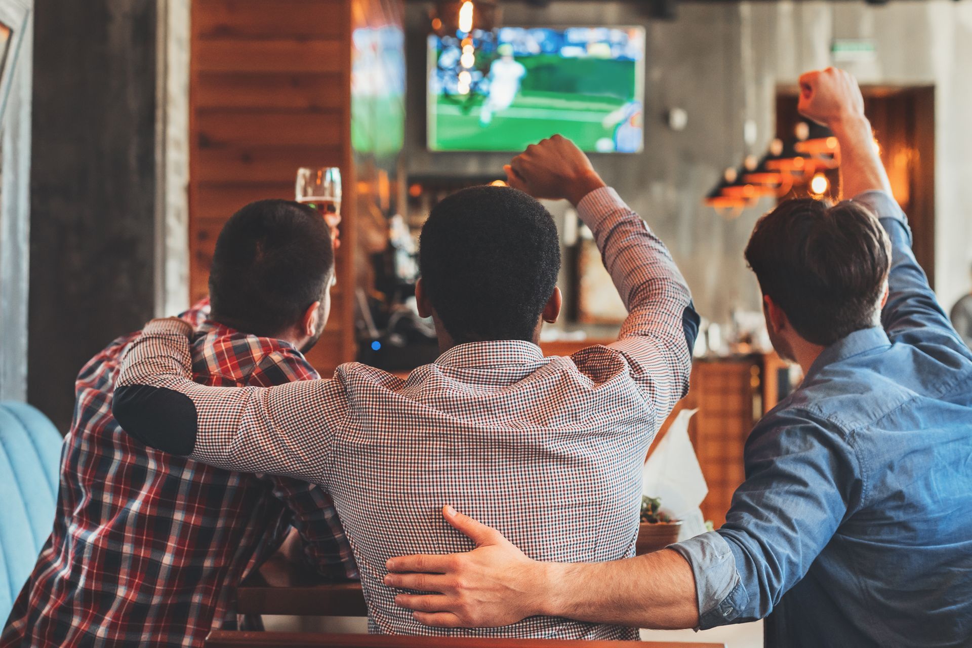 Three people cheering, watching a sports game on TV in a bar. Three people cheering, watching a sports game on TV in a bar.
