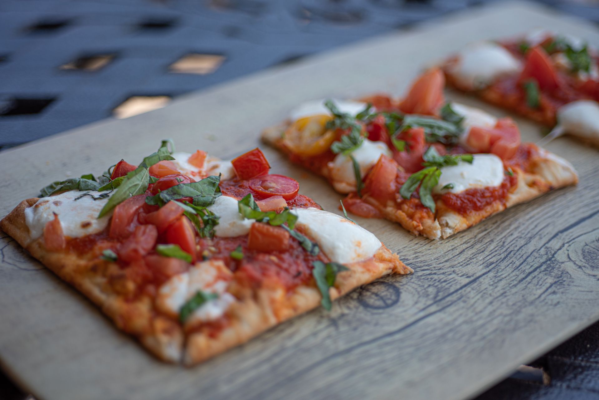 Two rectangular flatbread pizzas topped with tomato, fresh mozzarella, and basil on a light wooden serving board.