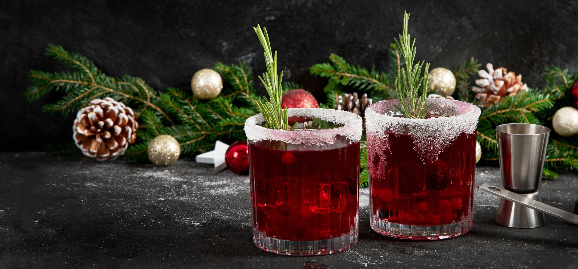 Two cranberry cocktails with rosemary, salt rim, Christmas decor on dark surface.