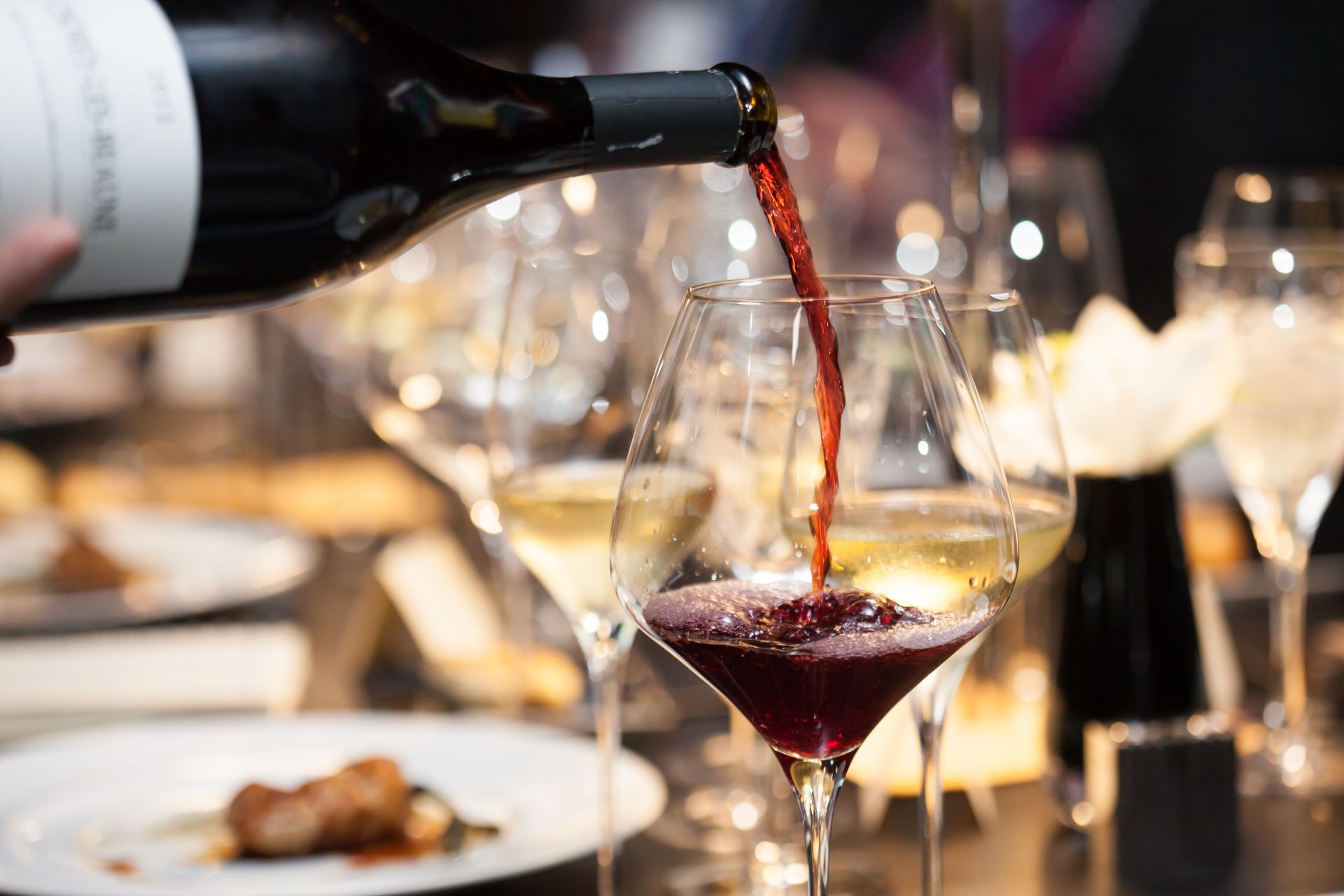Red wine being poured into a glass at a candlelit dinner table