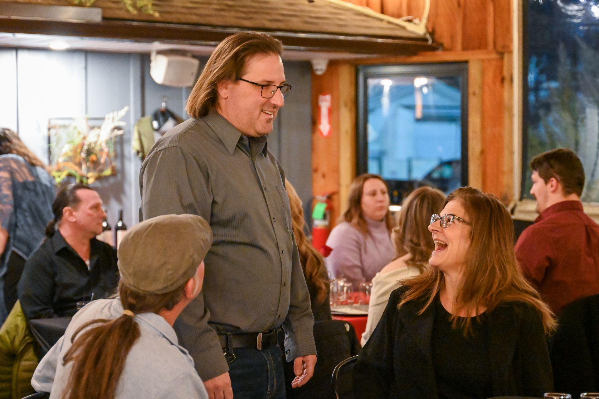 A man is standing in front of a group of people sitting at tables in a restaurant.