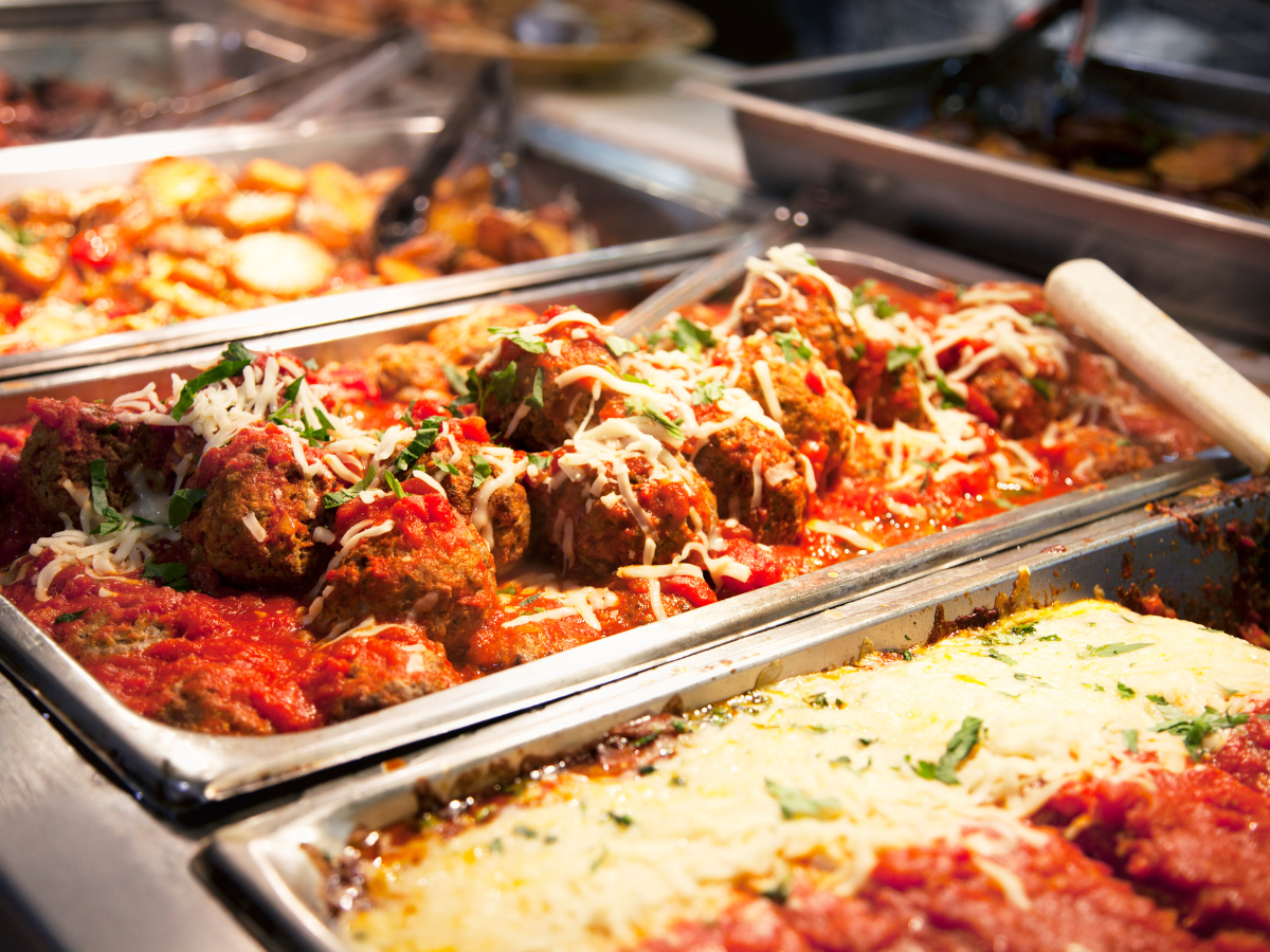 Meatballs in tomato sauce topped with cheese in a buffet tray, other dishes in the background.