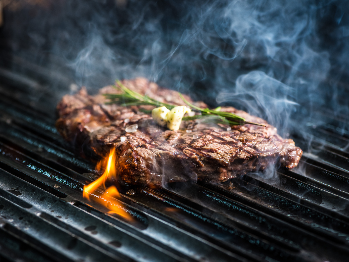 A steak is cooking on a grill with smoke coming out of it.