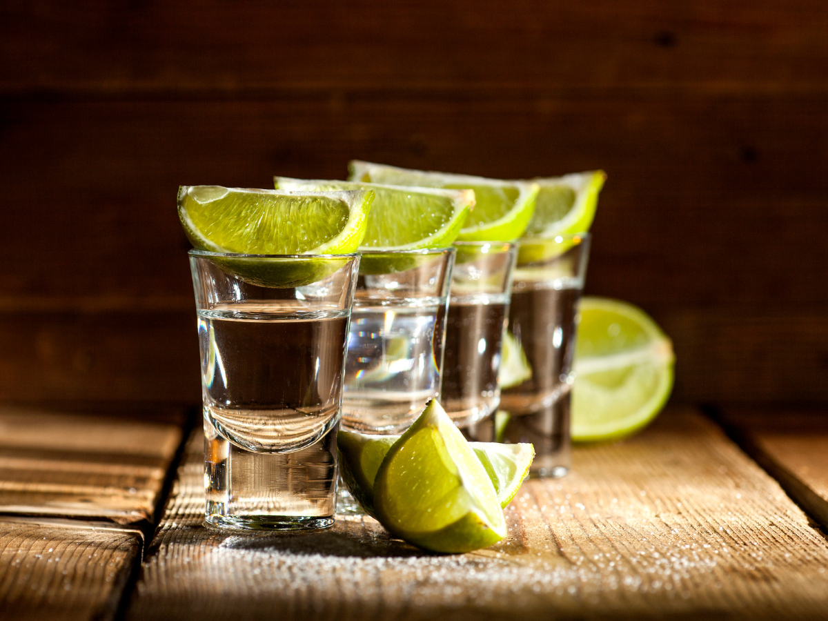 Tequila shots with lime wedges on a rustic wooden surface, illuminated by warm light. Tequila shots with lime wedges on a rustic wooden surface, illuminated by warm light.