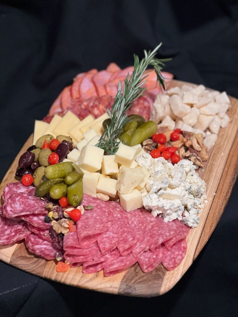 A wooden cutting board filled with meats , cheeses , olives , pickles and nuts from Happy Hour Bar & Grill.