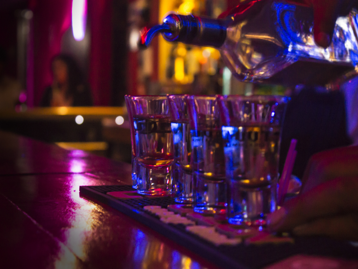 Row of shots on a bar, lit with purple and blue lights, near a tap.