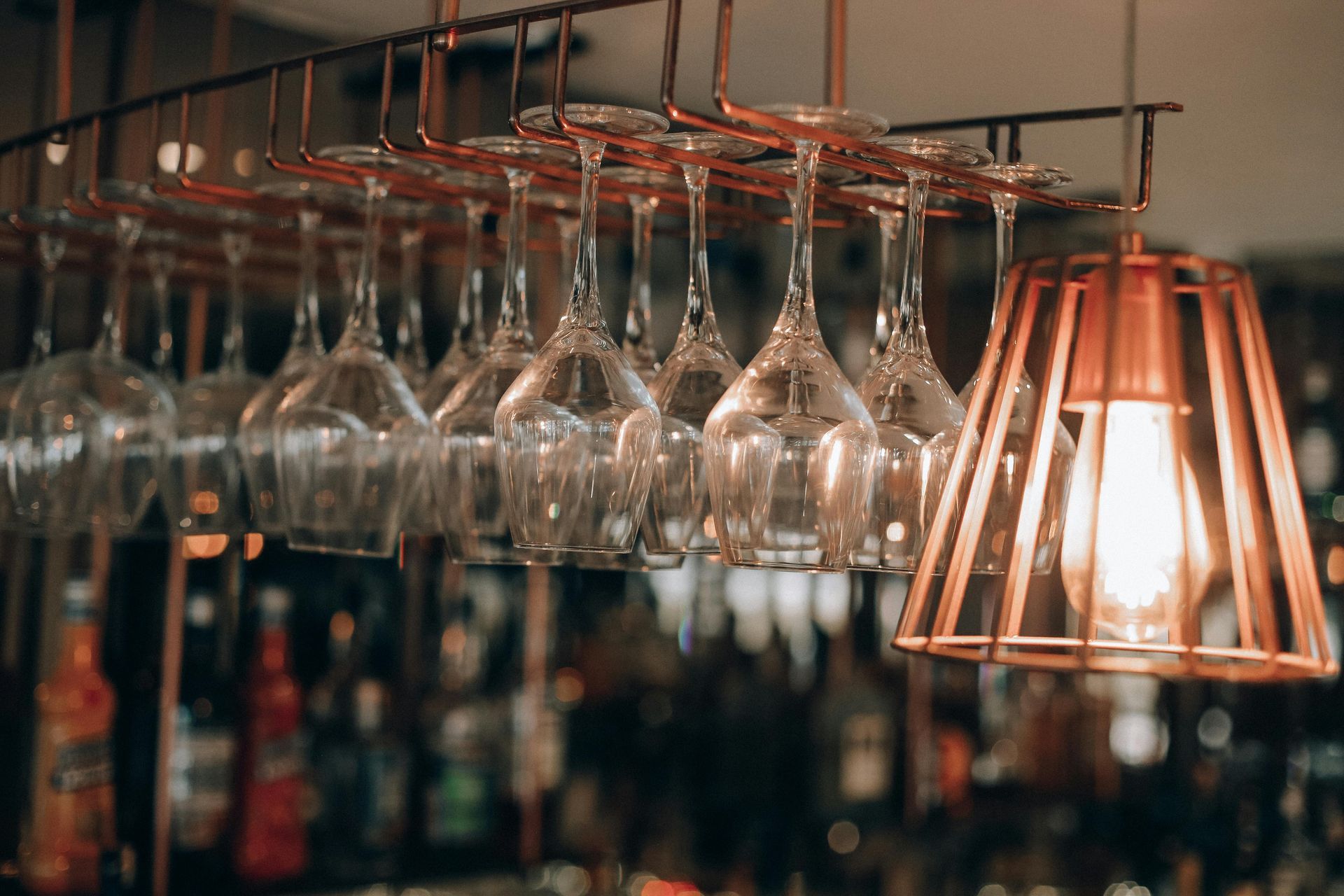 A row of wine glasses hanging from a rack in a bar.