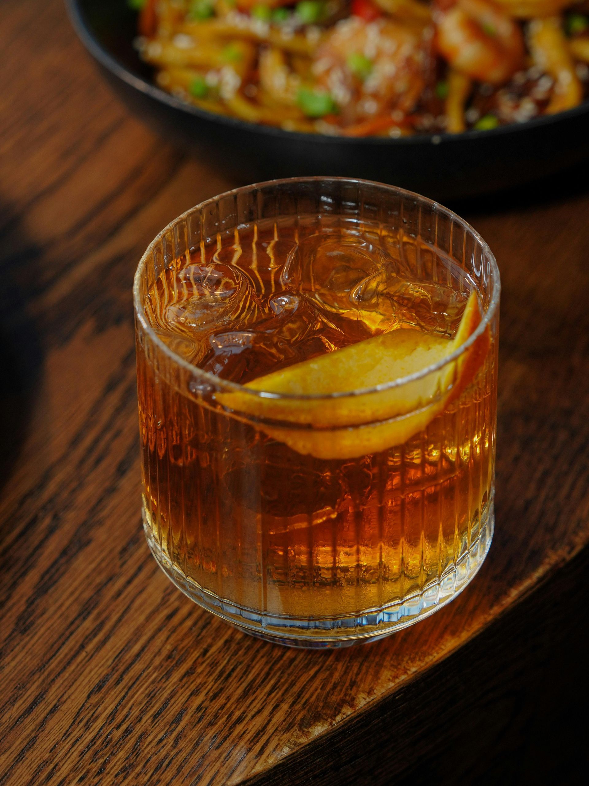 A glass of whiskey with ice and a slice of lemon on a wooden table.