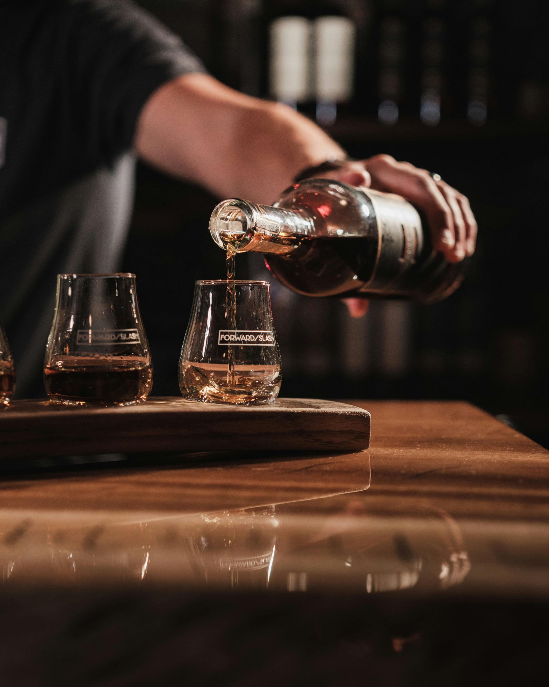 A person is pouring a drink into a glass on a wooden table.