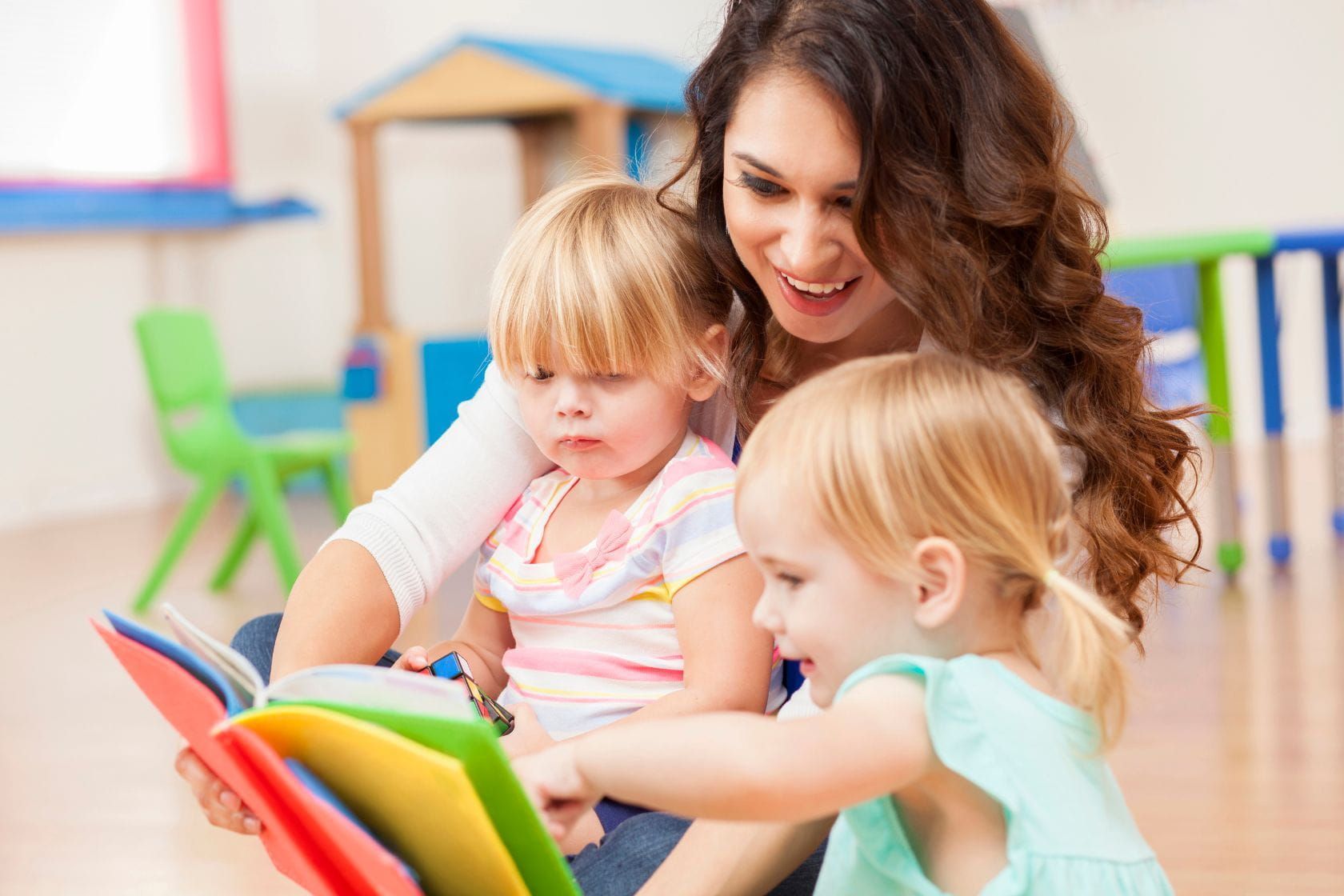 Teacher reading with young children, modeling attentive adult presence in early learning.
