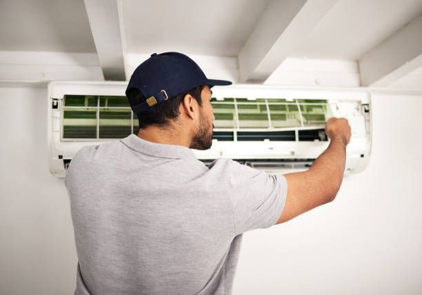 A man wearing a hat is cleaning an air conditioner.   — Phoenix, AZ — Trutek Air Conditioning and Heating LLC