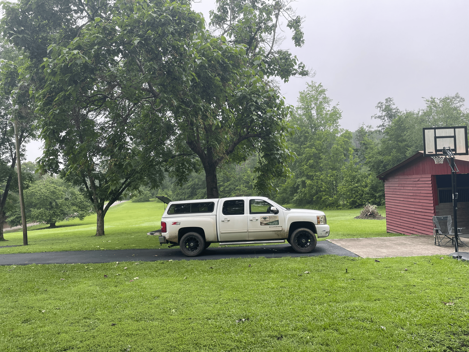 White truck parked on a driveway in a grassy yard, with trees and a red shed in the background.