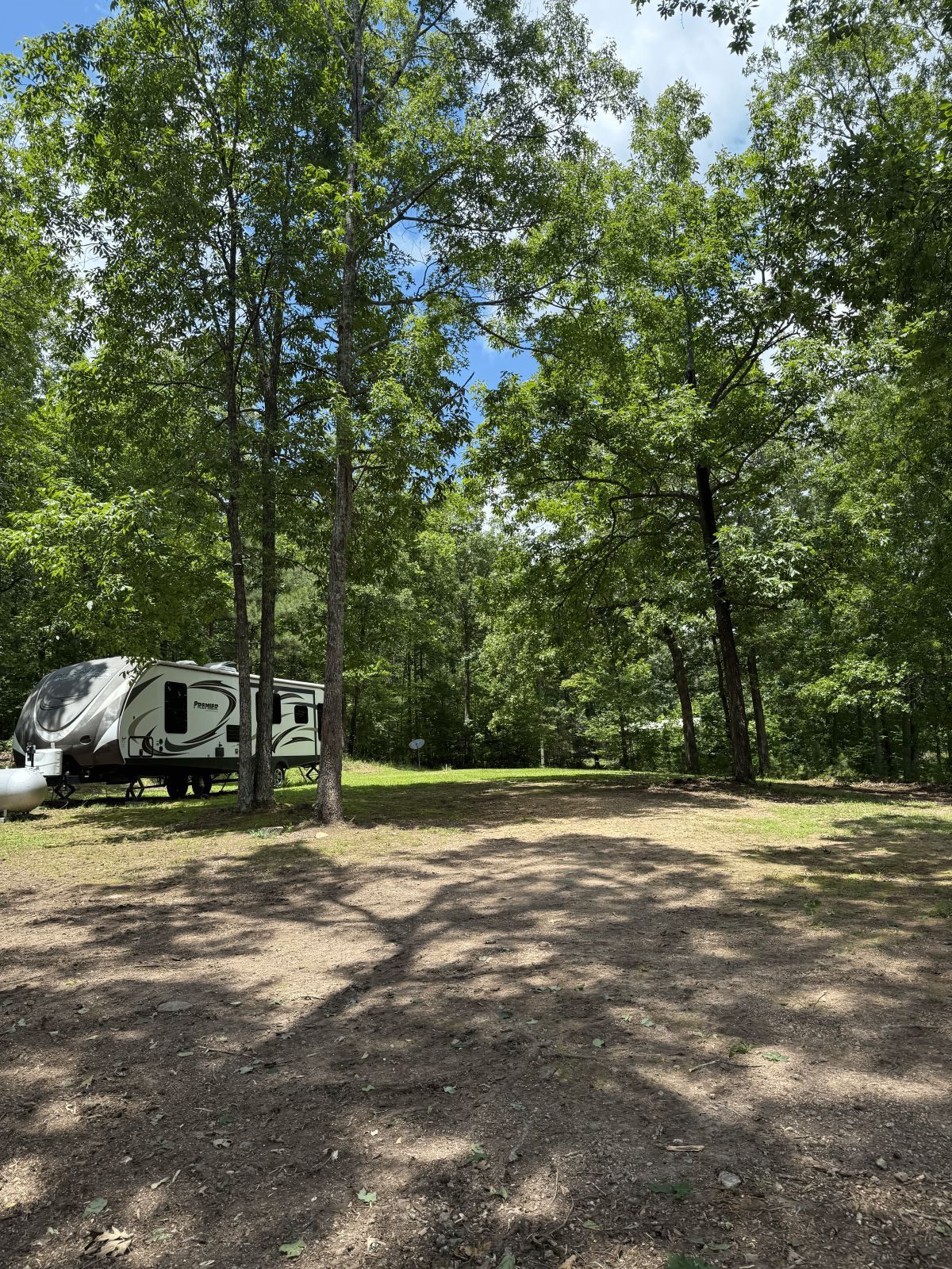 A camping scene with a trailer parked in a clearing surrounded by trees, blue sky peeking through.
