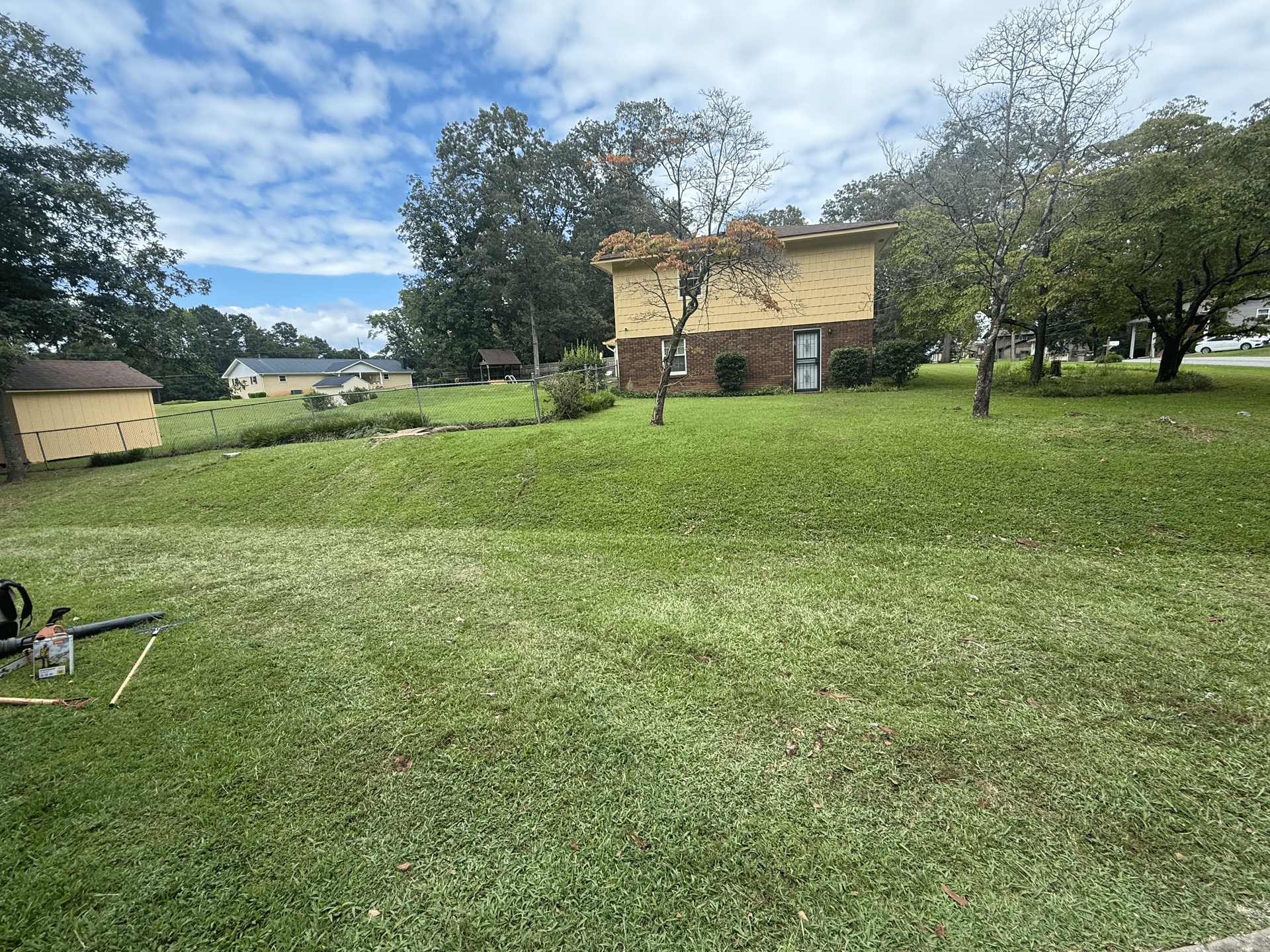 Lawn with a small building, partly obscured by trees. Blue sky with clouds.