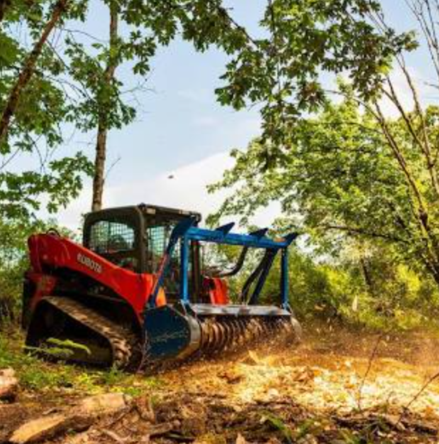 Red and blue Kubota tractor clearing brush in a wooded area.