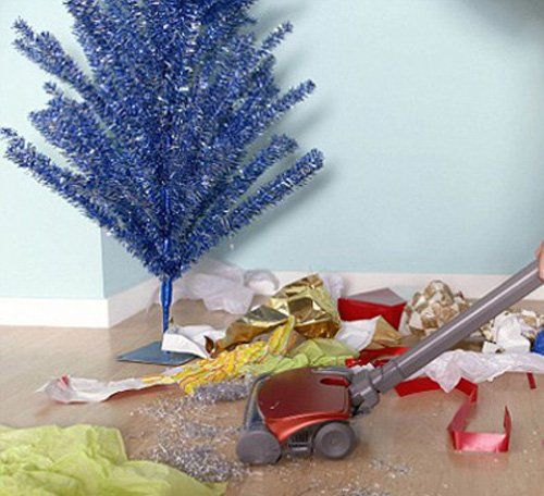 A vacuum cleans up mess from Christmas with wrapping paper on floor and a blue tree