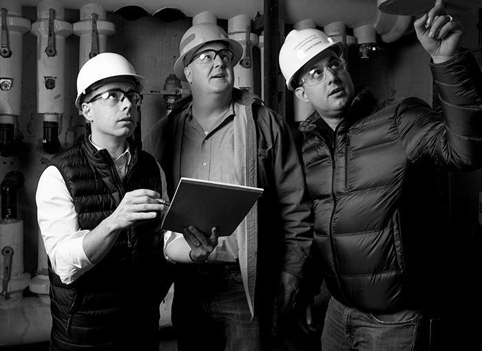 Three engineers wearing hard hats inspecting equipment in a mechanical room.